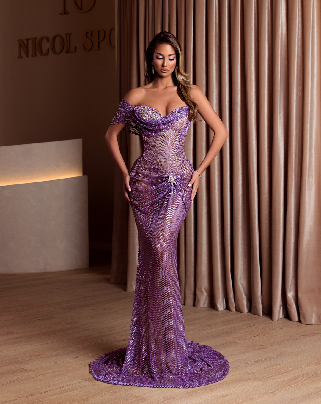 Woman in a purple evening gown standing in front of a curtain with 'Nicol Spence' branding.