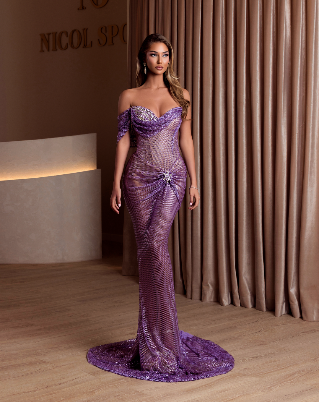Woman in a purple evening gown standing in front of a curtain.