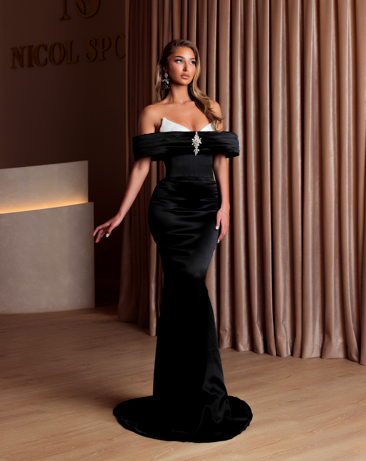 Woman in a black and white evening gown standing in front of a curtain.
